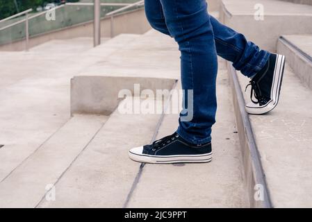 primo piano di un paio di gambe dell'uomo in sneakers nere che scendono le scale di cemento. concetto urbano. Foto Stock