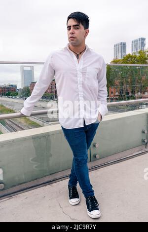 Attraente giovane uomo latino in pantaloni scuri e una camicia bianca in una scena urbana. Attraente giovane uomo latino in pantaloni scuri e una camicia bianca in una città Foto Stock