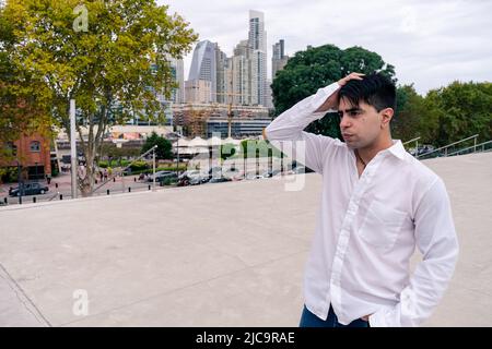 Attraente giovane uomo latino in pantaloni scuri e una camicia bianca in una scena urbana. Attraente giovane uomo latino in pantaloni scuri e una camicia bianca in una città Foto Stock