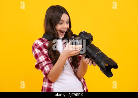 Stupito adolescente. Ragazza adolescente con fotocamera dslr con obiettivo zoom. Fotografo bambino isoallato su sfondo giallo. Scuola di fotografia. Riprese con Foto Stock