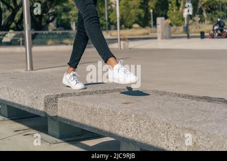 Gambe femminili sottili in sneakers bianche che saltano tra blocchi di cemento in un quadrato. Concetto divertente tempo. Foto Stock