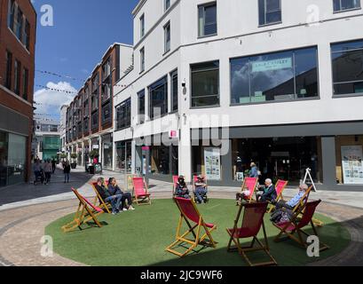 Newbury, berkshire, Inghilterra, Regno Unito. 2022. Sedie a sdraio in erba per gli amanti dello shopping nel centro città. Foto Stock