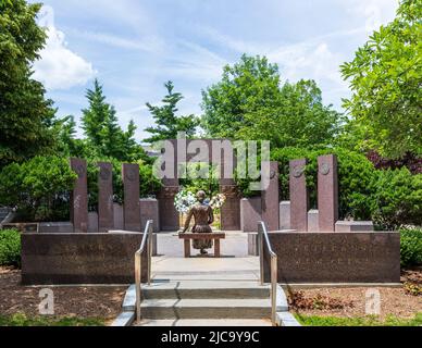 ASHEVILLE, NC, USA-5 GIUGNO 2022: Il Memoriale dei Veterani del North Carolina Occidentale in Piazza del pacchetto include la statua della donna sulla lettera di lettura della panchina. wrea floreale Foto Stock