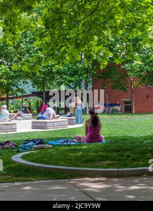 ASHEVILLE, NC, USA-5 GIUGNO 2022: La giovane donna meditating in piazza del pacchetto, altre persone a distanza. Foto Stock