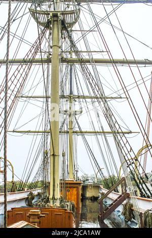 Primo piano dell'armamento di un'alta nave a vela in legno con un ponte di legno lucido bagnato contro il cielo coperto Foto Stock