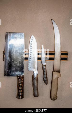 Quattro coltelli da chef ben utilizzati su un supporto magnetico montato su pareti testurizzate Foto Stock