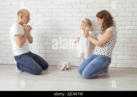 Il bambino con gli apparecchi acustici e gli impianti cocleari gioca con i genitori sul pavimento. Concetto di sordi e riabilitazione e diversità Foto Stock