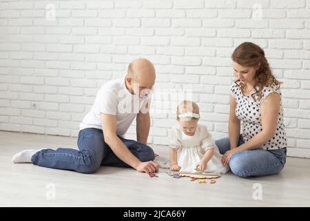Il bambino con gli apparecchi acustici e gli impianti cocleari gioca con i genitori sul pavimento. Concetto di sordi e riabilitazione e diversità Foto Stock