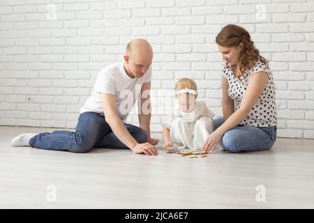 Il bambino con gli apparecchi acustici e gli impianti cocleari gioca con i genitori sul pavimento. Concetto di sordi e riabilitazione e diversità Foto Stock