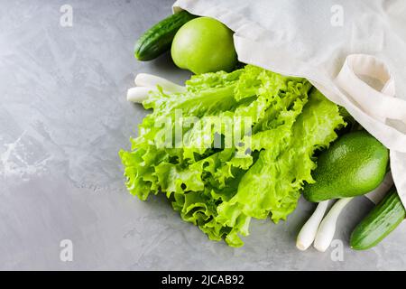 Verdure e frutta verdi, verde in borsa di cotone shopping. Borsa di lino ecologico con frutta e verdura verdi su sfondo grigio. Il consumo è ragionevole Foto Stock