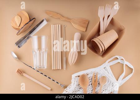 Posate in legno, stoviglie usa e getta in carta e utensili da bar su sfondo beige. Utensili da cucina ecologici e borsa a rete. Senza sprechi, senza plastica c Foto Stock