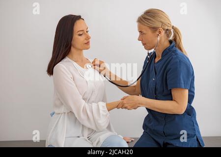 Medico curante uso stetoscopio esame della frequenza cardiaca del paziente alla consultazione in ospedale Foto Stock