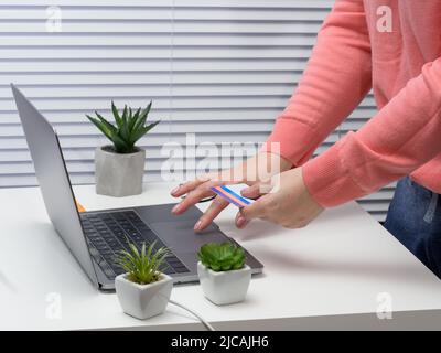 donna in un maglione rosa effettua acquisti online con un laptop, una carta di credito in mano. Foto Stock