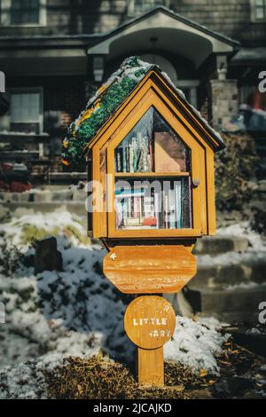 Piccola biblioteca in quartiere in pole nel cortile di fronte con decorazioni natalizie di fronte a casa con neve a terra Foto Stock