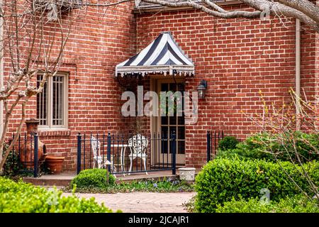 Piccolo patio con ringhiere in ferro su casa di mattoni - tenda a stirare sulla porta con corona e chiminea e bianco ferro bistro set - paesaggistica Foto Stock