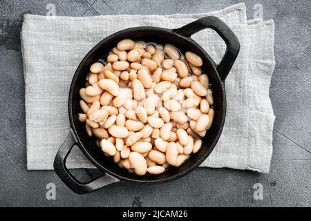 Fagioli bianchi in scatola, in padella in ghisa, su sfondo in pietra grigia, vista dall'alto, piatto Foto Stock