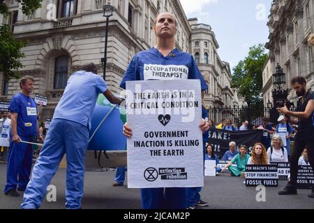 Londra, Regno Unito. 11th giugno 2022. Un manifestante tiene un cartello che dice "l'inazione del governo sta uccidendo la Terra" durante la manifestazione fuori Downing Street. Estinzione medici, infermieri e altri professionisti della ribellione si sono riuniti per una protesta a Westminster per chiedere la fine degli investimenti nei combustibili fossili. (Foto di Vuk Valcic/SOPA Images/Sipa USA) Credit: Sipa USA/Alamy Live News Foto Stock