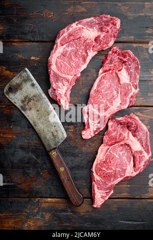 Bistecca cruda di carne marmorizzata con sale, rosmarino e aglio, e vecchio coltello da macellaio, su un vecchio sfondo di legno scuro, vista dall'alto, piatto Foto Stock
