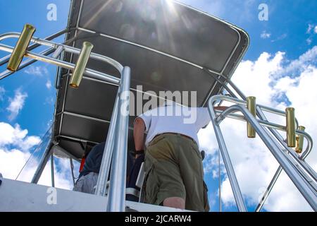 VEW con razzi solari dal basso di due uomini irriconoscibili sul ponte superiore di una barca da pesca charter contro un cielo molto blu Foto Stock