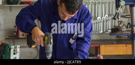 Immagine di un uomo in officina che restaura i mobili fissando le viti con un cacciavite. Lavoro fai-da-te Foto Stock