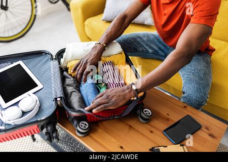 Primo piano mani di giovane africano uomo imballaggio bagagli prima di andare in vacanza Foto Stock
