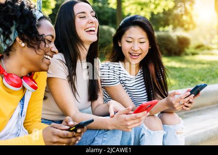 Giovane donna multirazziale amici divertirsi utilizzando i telefoni cellulari in strada Foto Stock