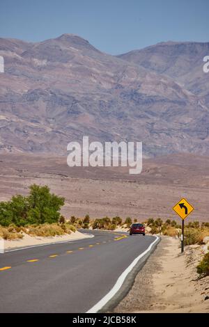 Auto rossa che fa svolta affilata su strada lastricata nel deserto che conduce alle montagne Foto Stock