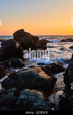 Tramonto sulla spiaggia di grandi rocce ricoperte di cozze Foto Stock