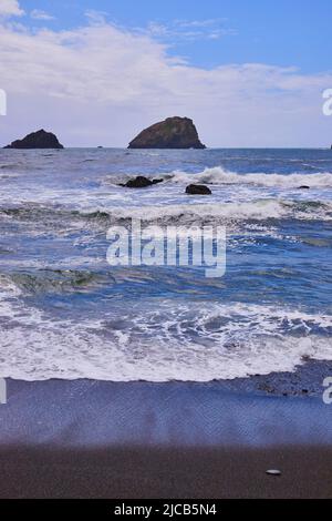 Onde morbide che colpiscono la spiaggia di sabbia nera sulla costa occidentale Foto Stock