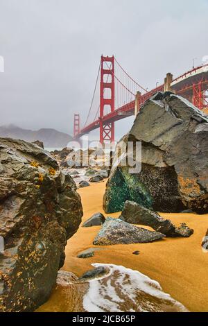 Rocce che coprono la spiaggia sabbiosa in mattinata di nebbia presso il Golden Gate Bridge a San Francisco Foto Stock