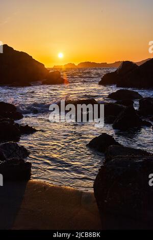 Spiaggia di sabbia con onde sulle rocce vicino al tramonto vibrante Foto Stock