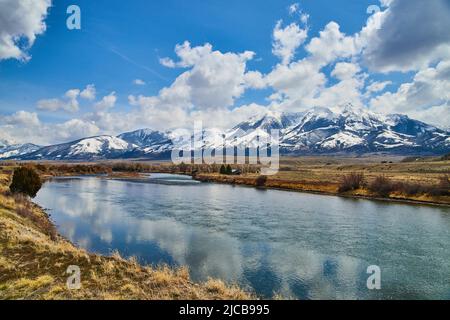 Fiume e campi in primavera con incredibili montagne innevate all'orizzonte Foto Stock