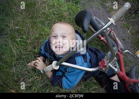 Ragazzo in via terra con un infortunio al ginocchio urlando dopo la caduta alla sua bicicletta Foto Stock