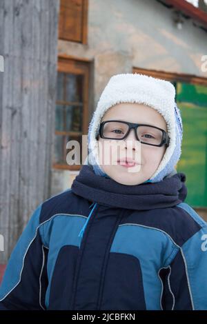 Ritratto di ragazzo piccolo carino in abiti invernali con neve che cade. I bambini si divertono e catturano i fiocchi di neve, all'aperto nelle giornate fredde. Foto Stock