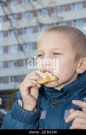 Il ragazzo mangia con gli occhi un pezzo di pane chiuso Foto Stock