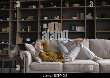 Donna di mezza età che si rilassa su un comodo divano nel soggiorno Foto Stock