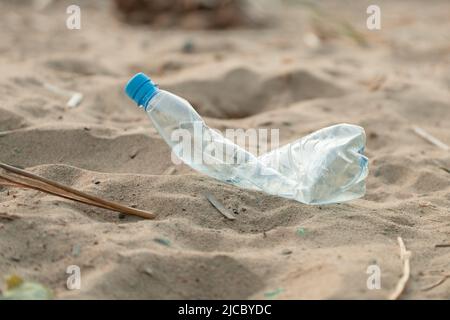 Blu vecchio schiacciato schiacciato schiacciato bottiglia di plastica vuota gettata sulla spiaggia sabbiosa. Problema ecologico, riciclaggio terra giorno. Foto Stock