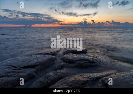 Massi e rocce nel surf sulla costa del Mar Baltico al tramonto, lunga esposizione Foto Stock