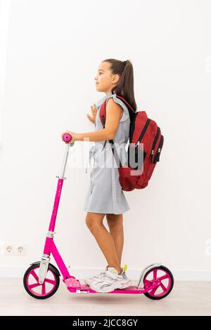 Lunghezza piena ripresa di profilo di una scolaretta con uno zaino in sella a un scooter isolati su sfondo bianco Foto Stock
