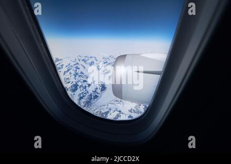 Vista dalla finestra dell'aeroplano durante il volo sopra le montagne innevate della Groenlandia. Foto Stock