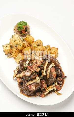 costolette di manzo stufato e funghi in salsa con patate arrosto su sfondo bianco Foto Stock