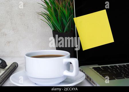 Nota adesiva su un notebook o notebook con schermo nero con altri accessori e caffè su un tavolo bianco. Foto Stock