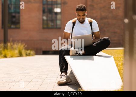 Concetto di freelance. Uomo afroamericano che usa un computer portatile, studia o lavora all'aperto, seduto nel parco cittadino Foto Stock