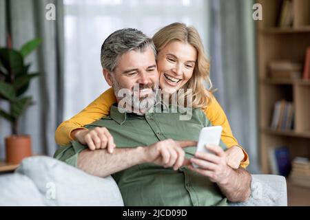 Coppia felice di mezza età che usa il telefono cellulare a casa insieme Foto Stock