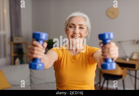 Sport domestici. Donna anziana felice che fa le esercitazioni di idoneità con i pesi, i manubri di tenuta e l'addestramento nel paese Foto Stock