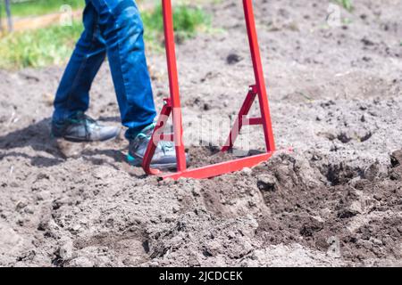 Un agricoltore in jeans scava il terreno con una pala a forcella rossa. Una pala miracolosa, uno strumento pratico. Coltivatore manuale. Il coltivatore è un han efficiente Foto Stock