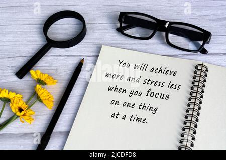 Citazione motivazionale sul libro della nota con lente d'ingrandimento sulla scrivania di legno bianco - raggiungerete più e meno sforzo quando vi concentrate su una cosa a ti Foto Stock
