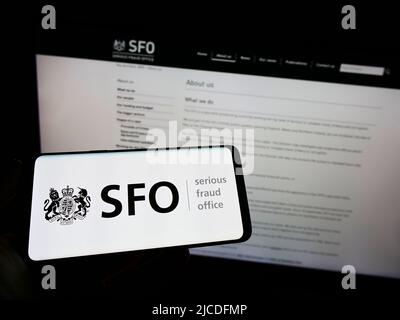 Persona che tiene uno smartphone con il logo dell'agenzia britannica Serious Fraud Office (SFO) sullo schermo di fronte al sito Web. Mettere a fuoco sul display del telefono. Foto Stock