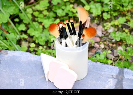 closeup il mazzo bianco marrone makeup kit spazzola con spugne palla nella scatola di plastica su sfondo verde marrone fuori fuoco. Foto Stock
