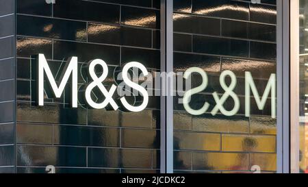 Marks & Spencer, Manchester Market Street, Inghilterra, Regno Unito. Cartello con logo M&S sulla parete di piastrelle scure riflessa nella finestra del negozio. Articoli di lusso per la casa, abbigliamento e cibo Foto Stock